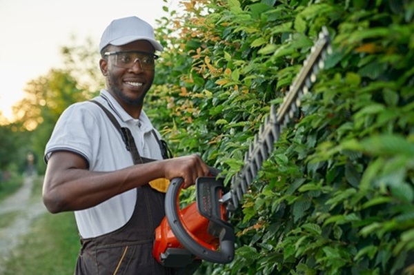 smiling afro gardener using hedge trimmer for cutting bushes